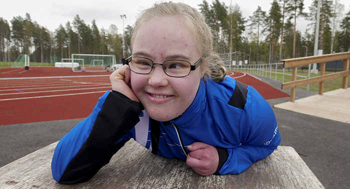 Roosa Kukkumäki hymyilemässä kameralle. On makuuasennossa penkillä.